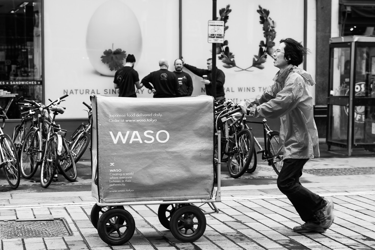 A person pushing a delivery trolley through London streets, black and white photo